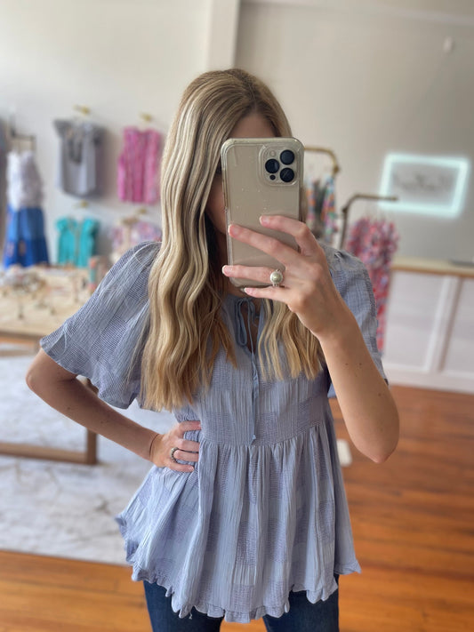 Woman taking a mirror selfie wearing a light blue striped blouse and dark jeans in a store.